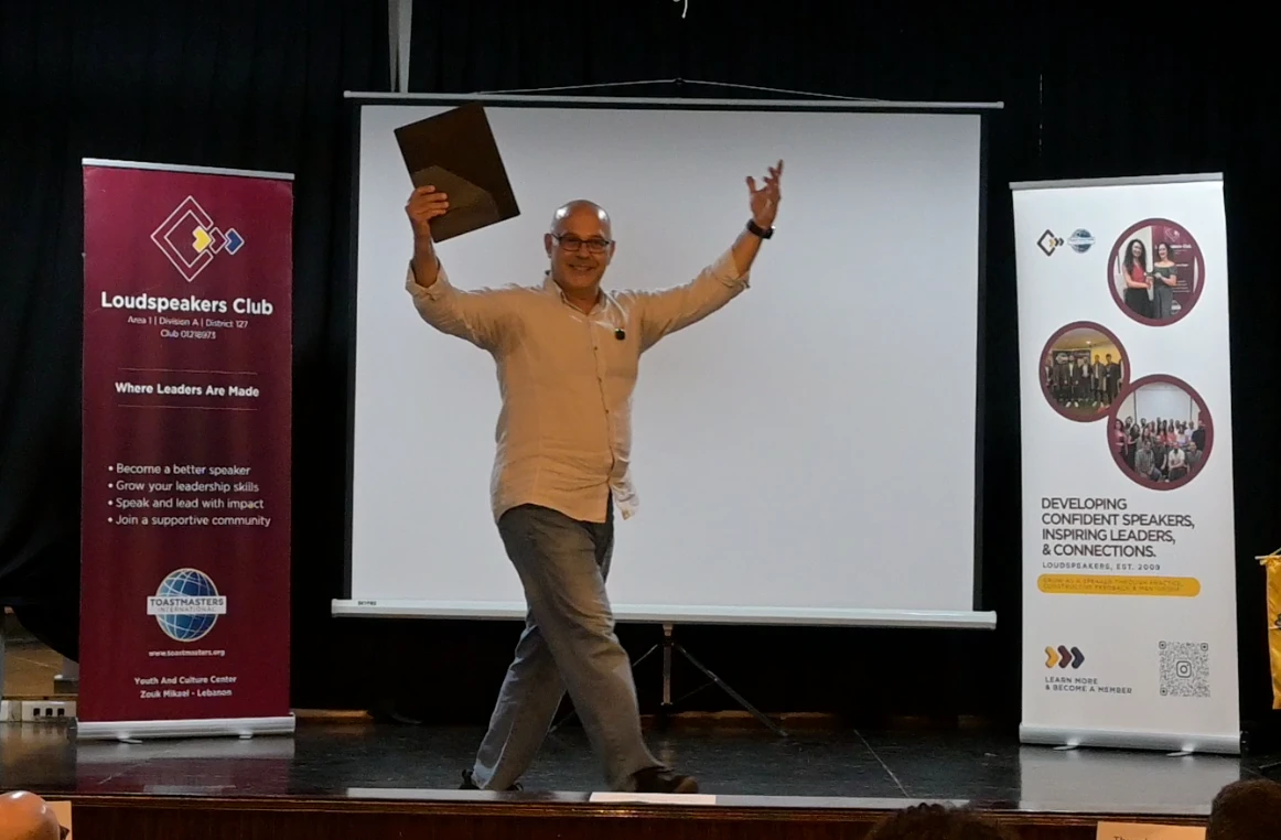 Elio Haddad presenting with energy on stage at Loudspeakers Toastmasters Club
